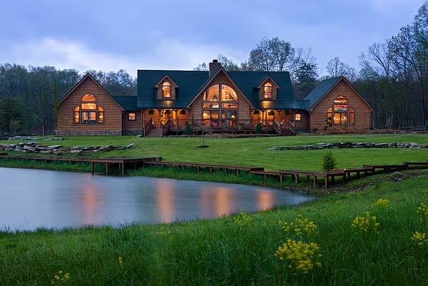 photo taken at dusk with lights on inside large estate log home. photo taken from across a pond